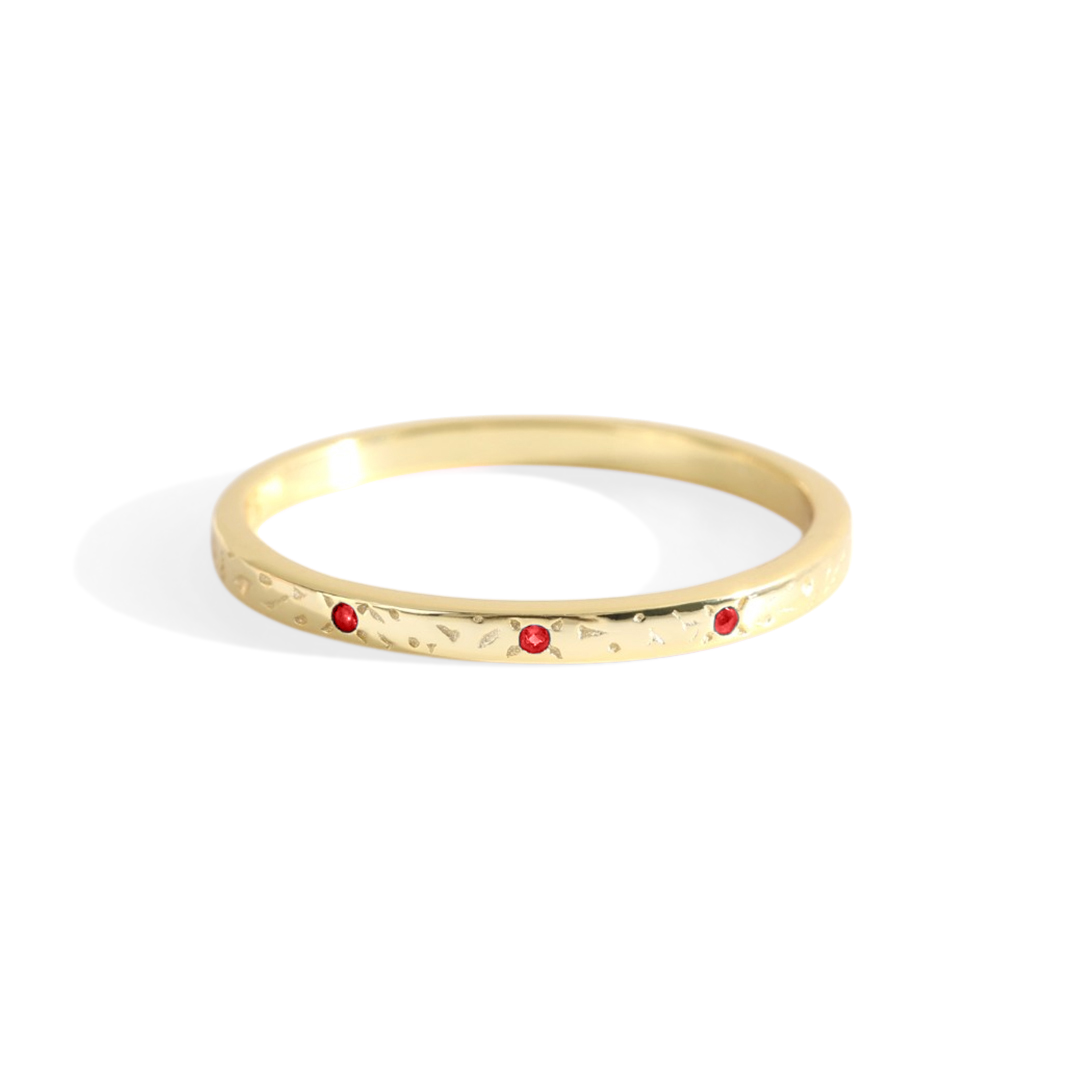 A thin gold band with red birthstones set at intervals along its length, displayed against a white background.