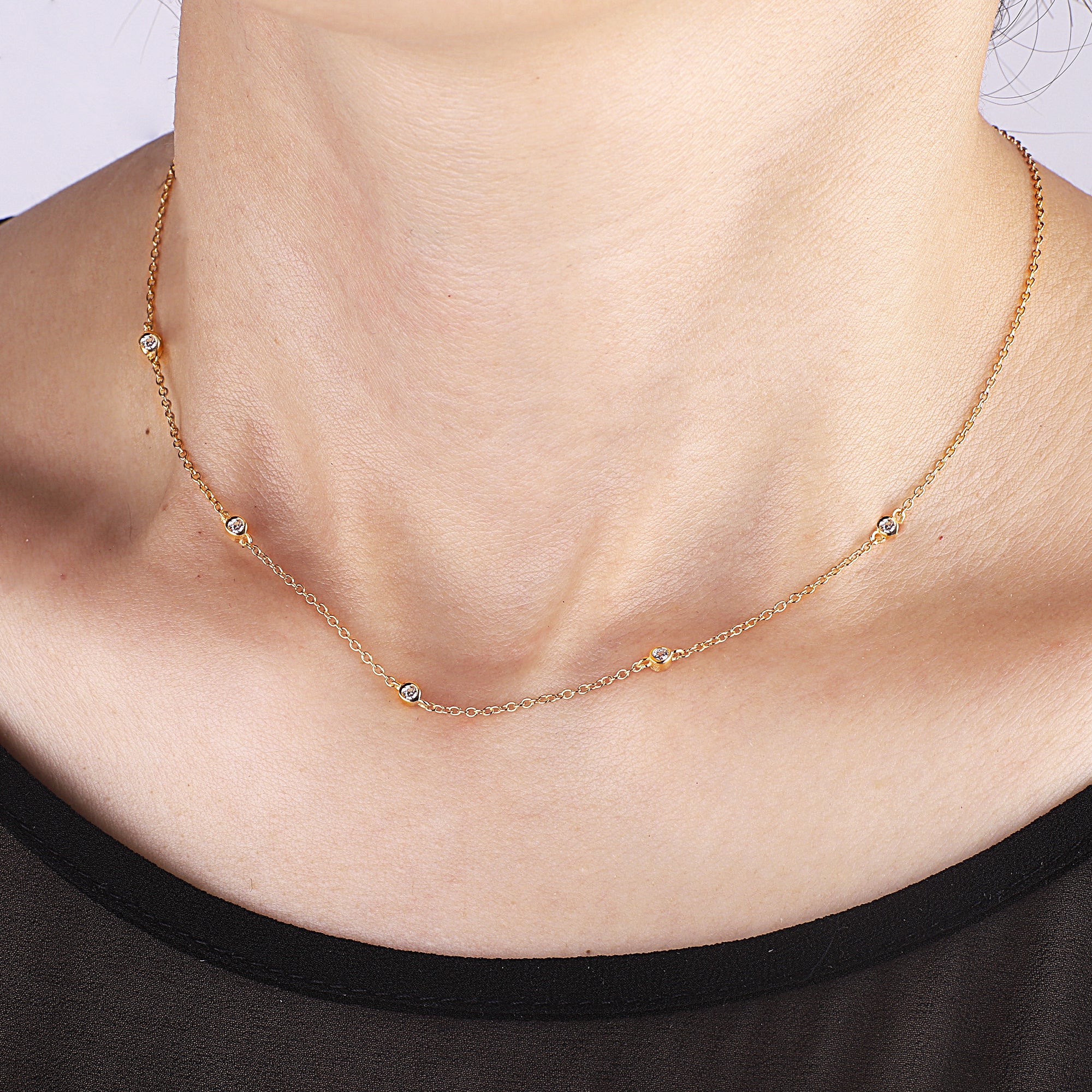 A five-crystal bezel-set necklace with gold plating on a person's neck.