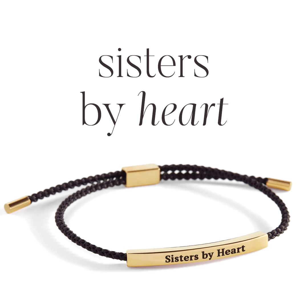 Bracelet with gold tag and 'Sisters by Heart' text on a light background