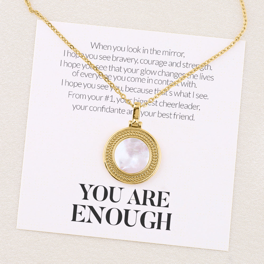 A gold-toned necklace with a pearl-like bead and a meaningful card attached, displayed against a neutral background.